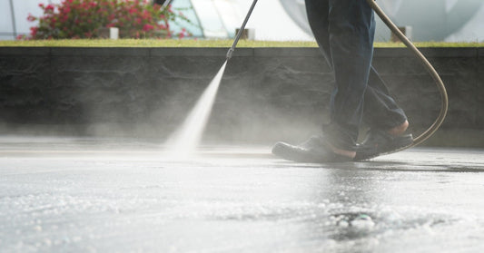 A contractor uses a pressure washer wand to spray water across a paved surface during an outdoor cleaning job.